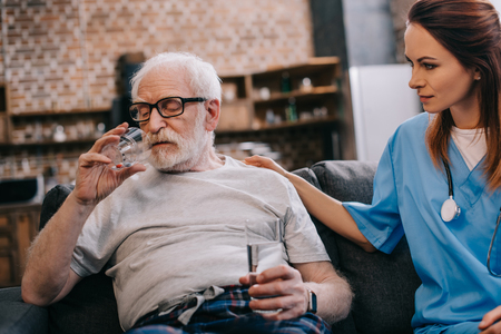 Nurse sitting by senior man taking medicationsの写真素材