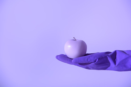 cropped view on hand in rubber glove holding purple apple, isolated on ultra violetの写真素材