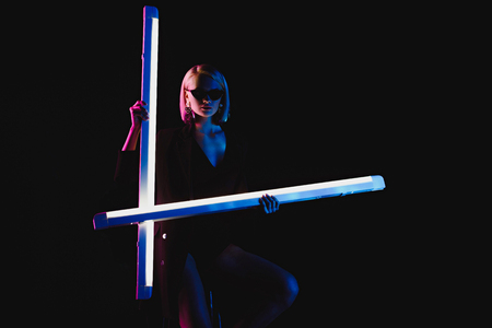 stylish trendy girl posing with two ultra violet lamps for fashion shoot, isolated on blackの写真素材