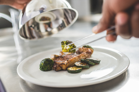 cropped image of african american chef decorating plate with food at restaurant kitchen