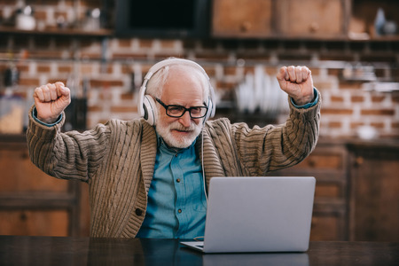 Excited elder man in headphones using laptop