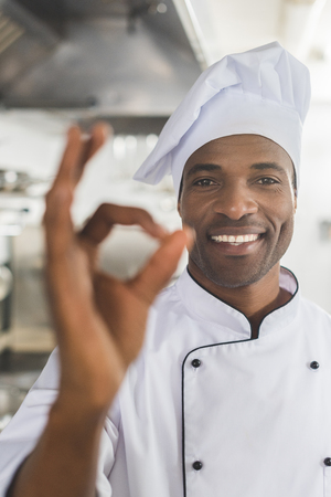 smiling african american chef showing okay gesture at restaurant kitchenの写真素材