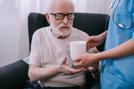 Nurse giving cup with drink to senior patient