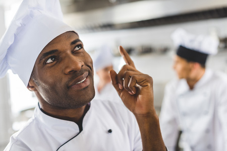 handsome african american chef pointing up at restaurant kitchenの写真素材