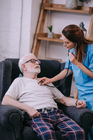 Nurse with stethoscope checking heartbeat of senior manの写真素材