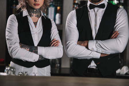 cropped image of female and male bartenders standing with crossed arms at bar