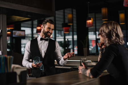 smiling bartender cleaning glass and talking with female visitorの写真素材