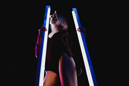 stylish girl posing with two ultra violet lamps for vogue shoot, isolated on black