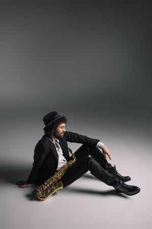 handsome musician sitting on floor with saxophoneの写真素材