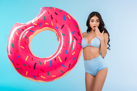 attractive shocked girl with inflatable donut ring, isolated on blueの写真素材