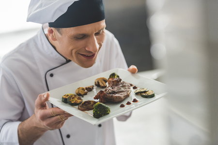handsome chef sniffing cooked steak with vegetables at restaurant kitchenの写真素材