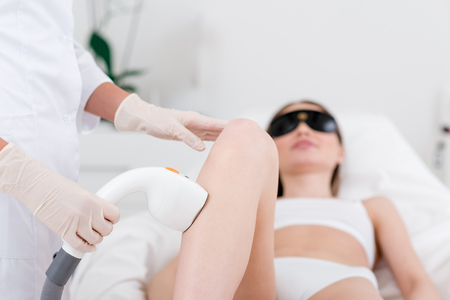 partial view of woman receiving laser hair removal epilation on leg in salonの写真素材
