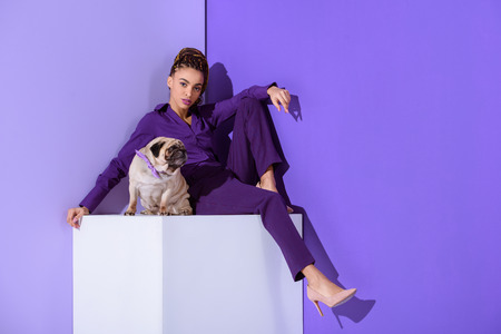 stylish mulatto girl in purple suit sitting on cube with pug dog, ultra violet trendの写真素材