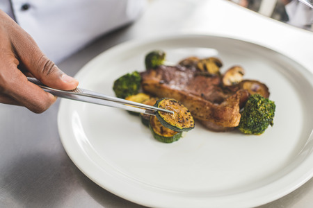 cropped image of african american chef putting piece of zucchini on plate at restaurant kitchen