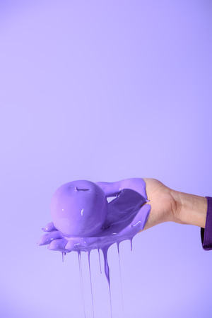 cropped view on female hand holding apple in purple paint, isolated on ultra violetの写真素材