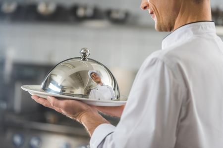 cropped image of handsome chef holding plate with lid at restaurant kitchenの写真素材