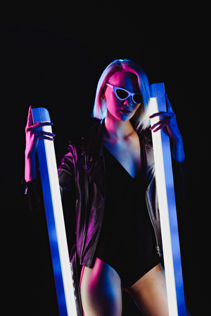 fashionable girl posing in sunglasses with two ultra violet lamps, isolated on blackの写真素材