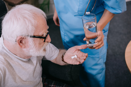 Nurse giving a glass of water to patient with pillsの写真素材