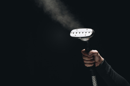 cropped shot of person holding garment steamer with steam on blackの写真素材
