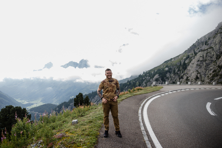 handsome young man standing on asphalt road in mountains and smiling at camera, Alpsの写真素材