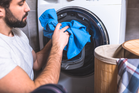 side view of loner putting laundry in washing machine in bathroomの写真素材