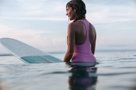 attractive woman sitting on surfboard in ocean at sunsetの写真素材