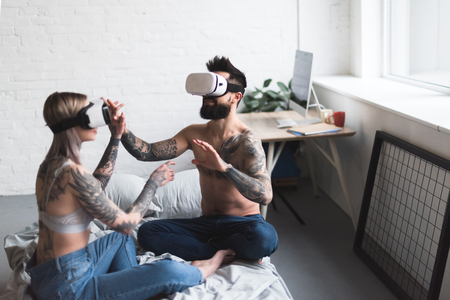 tattooed couple using vr headsets on bed at homeの写真素材