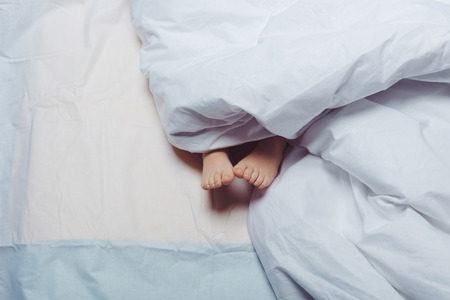 cropped shot of child feet underneath blanketの写真素材