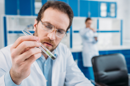 selective focus of scientist in white coat and eyeglasses looking at tube with reagent in hand in laboratoryの写真素材