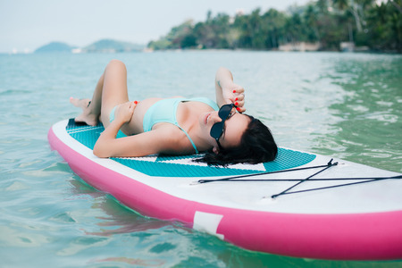 beautiful woman lying on paddle board on sea at tropical resortの写真素材