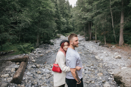 side view of happy young couple in love hugging near rapid mountain river in forestの写真素材