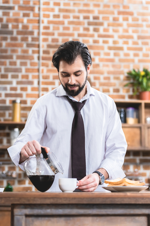 handsome loner businessman pouring coffee into cup at kitchenの写真素材