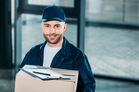 Young courier holding cardboard box with cargo declaration