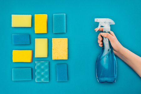 cropped image of woman holding spray bottle near washing sponges isolated on blueの写真素材
