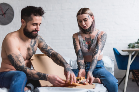 tattooed couple taking pizza on bed at homeの写真素材