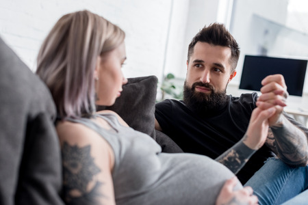 tattooed pregnant girlfriend and boyfriend holding hands at homeの写真素材