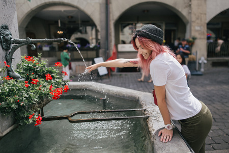 side view of happy young woman touching water in fountain on street in Bern, Switzerlandの写真素材