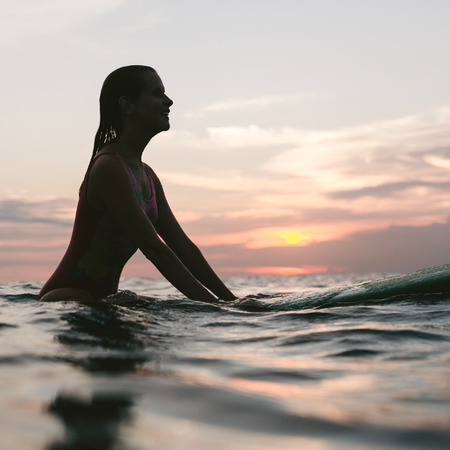 side view of silhouette of woman resting on surfing board in ocean on sunset