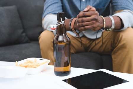 Close-up view of african american guy eating french fries with beer on table with digital tabletの写真素材