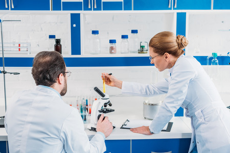 back view of scientists in white coats looking at tube with reagent in laboratory