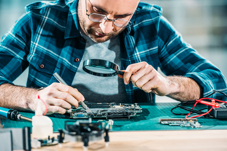 Repairman looking through magnifying glass while fixing circuit boardの写真素材