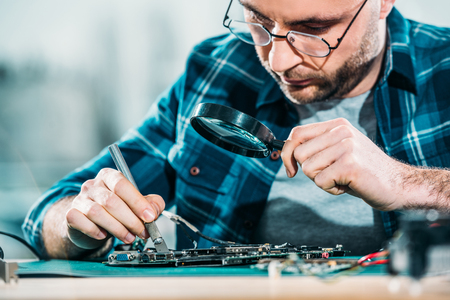Engineer fixing circuit board looking through magnifying glassの写真素材