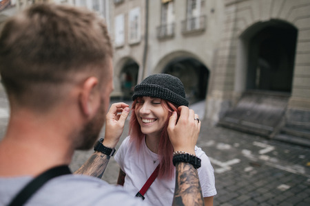 selective focus of man putting hat on beautiful smiling young woman while walking together on street...