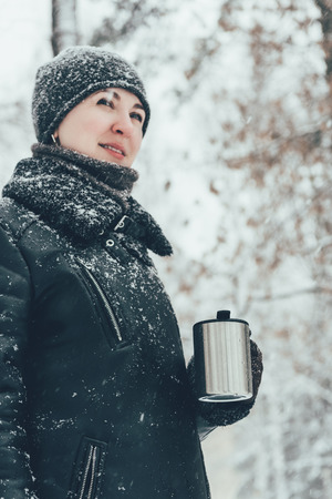 portrait of smiling woman with thermocup with hot drink looking away on street i winterの写真素材