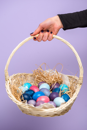 Female hand with Easter basket with colored eggs isolated on violetの写真素材
