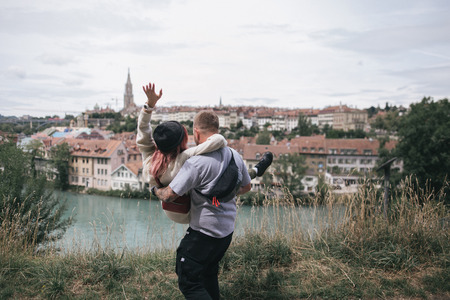 back view of young man carrying girlfriend and looking together at cityscape of Bern