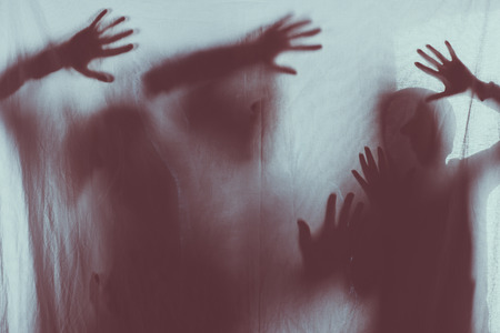 blurry scary silhouettes of people touching frosted glass with handsの写真素材