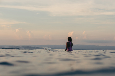 silhouette of surfer sitting on surfboard in sea at sunsetの写真素材