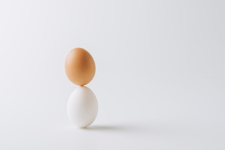 one white and one brown eggs stacked on white backgroundの写真素材