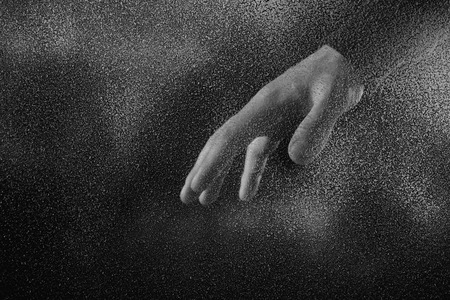 cropped shot of person showing hand through frosted glass in darknessの写真素材